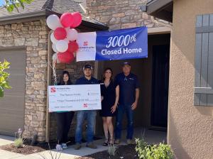 A group of people standing in front of a house holding a big check.