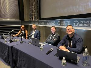 Noelle Kim, Jared Bauman, Randal Cumming, and James Allsworth seated at a table with their laptops at the DMLA conference