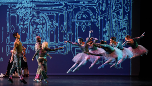 Hip Hop dancers wearing army fatigue inspired costumes face off with ballet dancers in tutus and pointe shoes in the battle scene against a large victorian backdrop