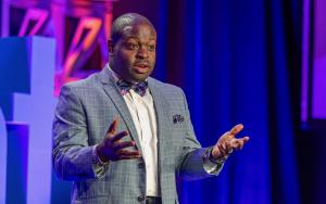 Man in a suit speaks from a conference stage