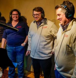 J. Blanton Plumbing CEO Aizik, Head of Marketing Cynthia, and Head of Digital Marketing Matt at a radio station recording their local ad, discussing services like fixing sewer lines, replacing water heaters, and expert Chicago plumbing solutions.